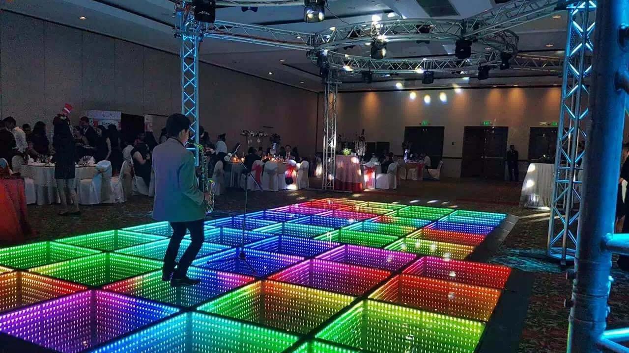 웨딩 연회장에서 색상 조명이 있는 3D 인피니티 LED 댄스 플로어 위에서 공연하는 색소폰 연주자