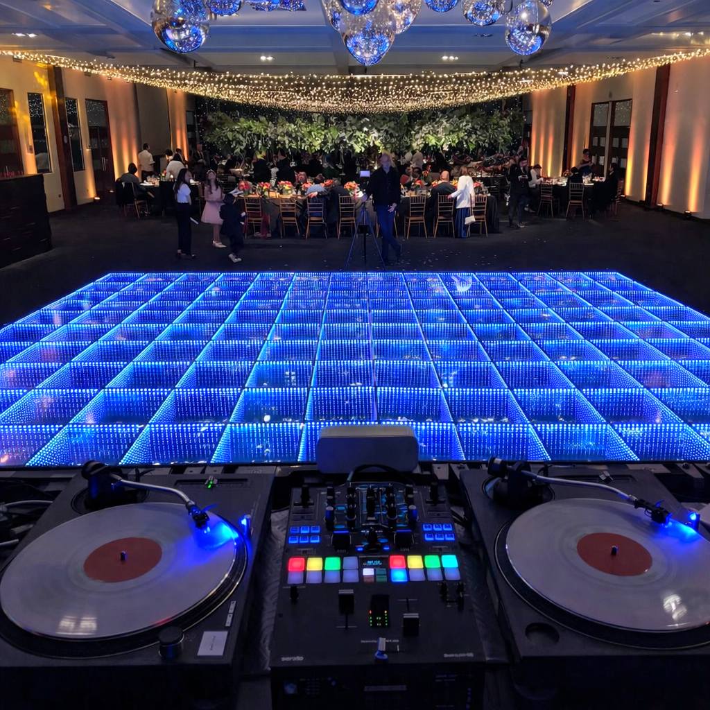 A blue 3D infinity LED dance floor viewed from a DJ booth with turntables at a formal indoor event.