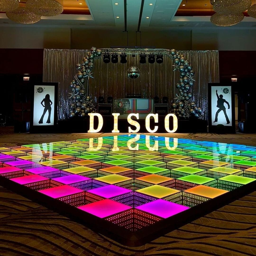 A 3D infinity mirror LED dance floor with a colorful glowing checkerboard pattern in front of a disco-themed event stage.
