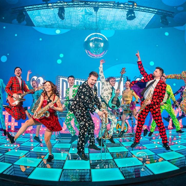 A live band performing on a glowing blue 3D infinity LED dance floor stage with a disco ball and colorful background.