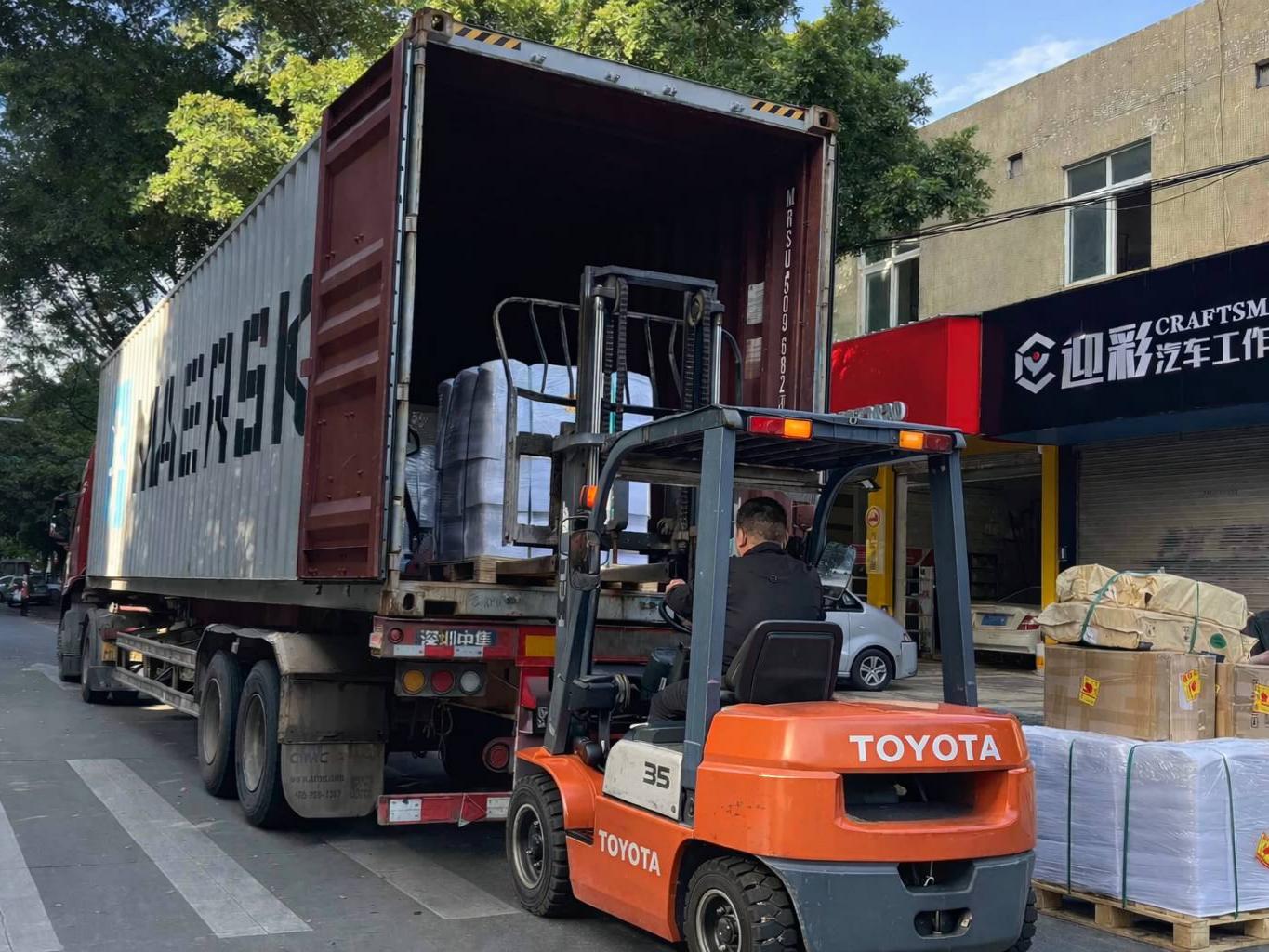 Un opérateur utilise un chariot élévateur Toyota orange pour charger des palettes de pistes de danse LED emballées en blanc dans un conteneur maritime Maersk destiné à l’exportation.