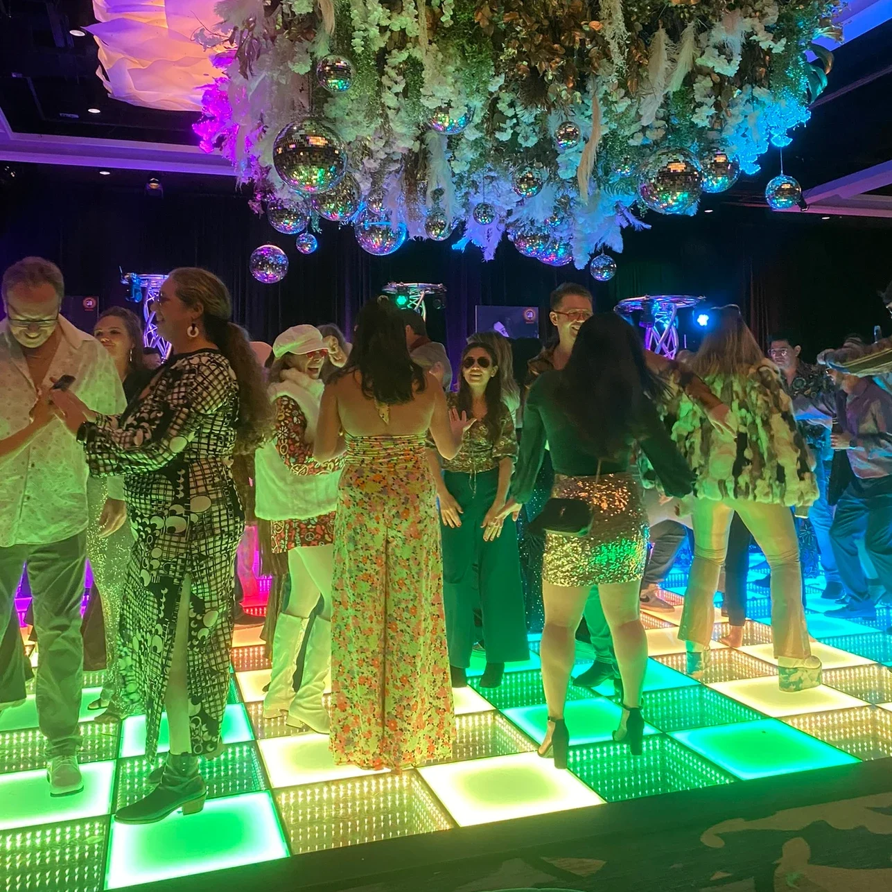 Une foule dansant sur une piste de danse LED 3D et colorée sous des boules disco lors d’une soirée animée en boîte de nuit.