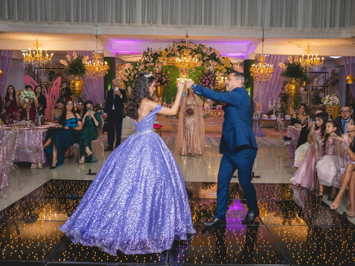 Young woman in a glittery purple dress dancing on a black LED starlit dance floor at a ceremony.
