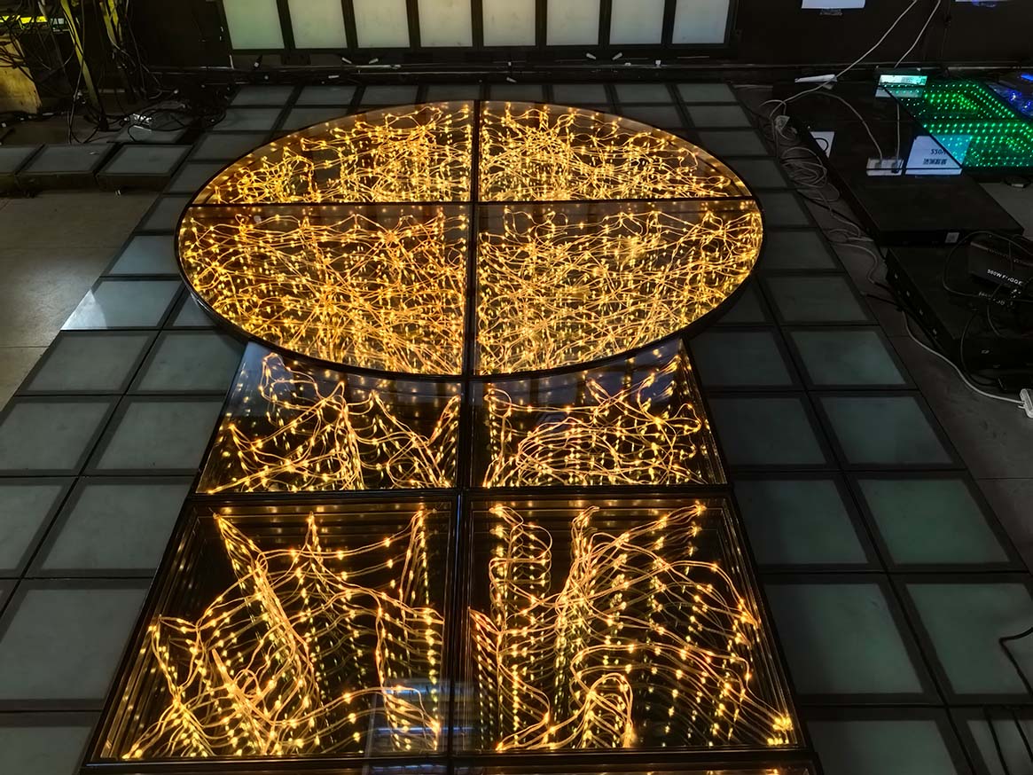 A custom T-stage and circular full-color starlit dance floor with warm gold lighting in a factory.