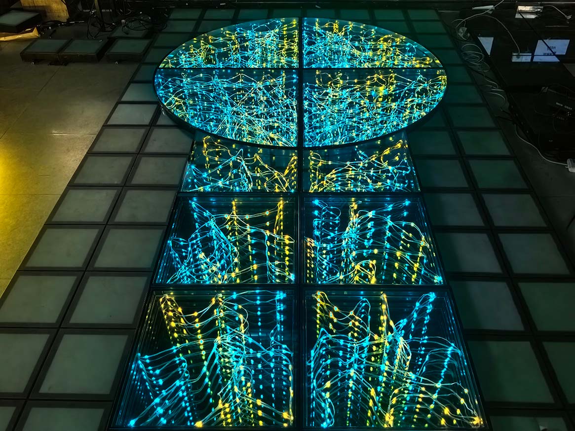A custom circular and T-stage full-color starlit dance floor with vibrant cyan and yellow lighting in a factory.