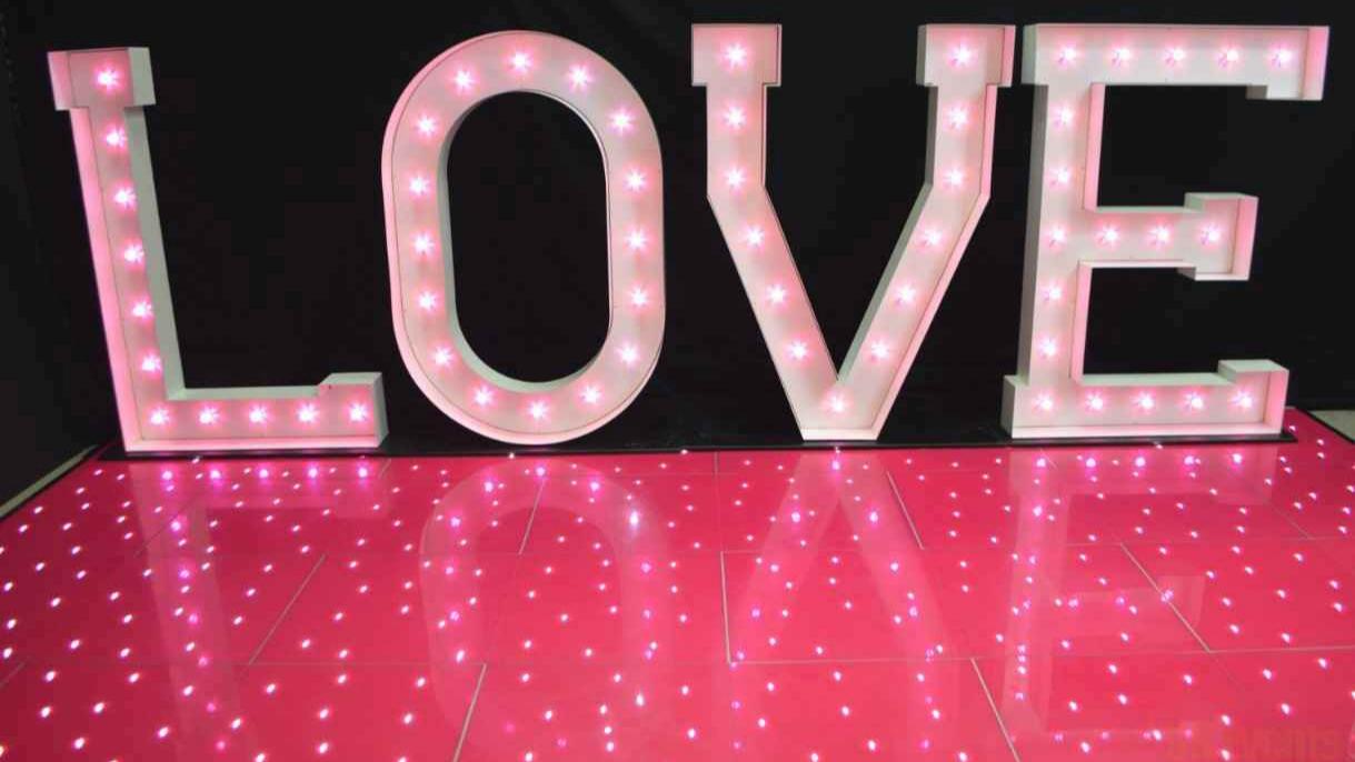 Large illuminated LOVE letters standing on a red LED starlit dance floor with twinkling lights for event decor.