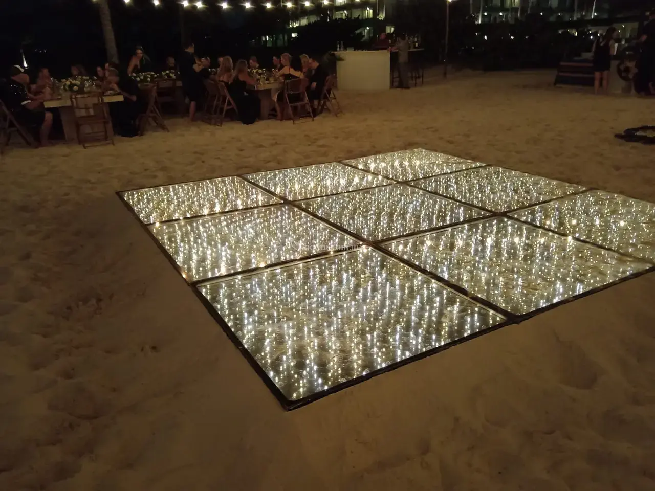 Un sol Piste de danse étoilée 3D brillant avec lumières blanches chaudes lors d’un dîner de plage en extérieur.