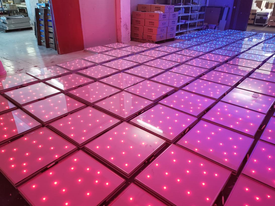 White LED starlit dance floor tiles emitting pink light during a quality test in a factory warehouse.