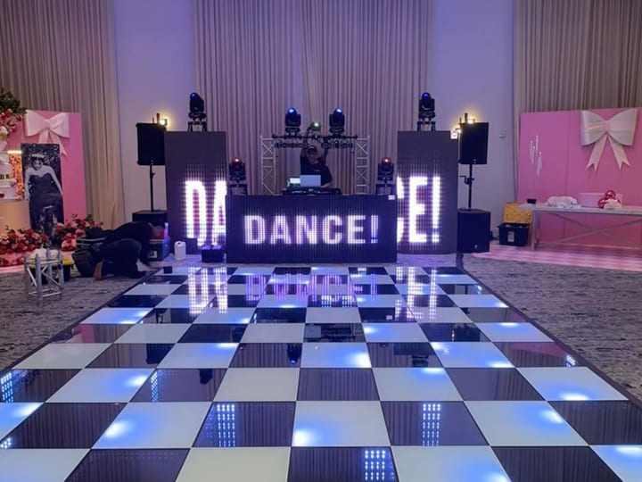 A checkerboard LED dance floor illuminated in front of a DJ booth for a wedding.