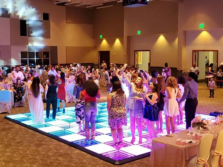 People dancing and taking photos on a glowing LED dance floor during a wedding event.