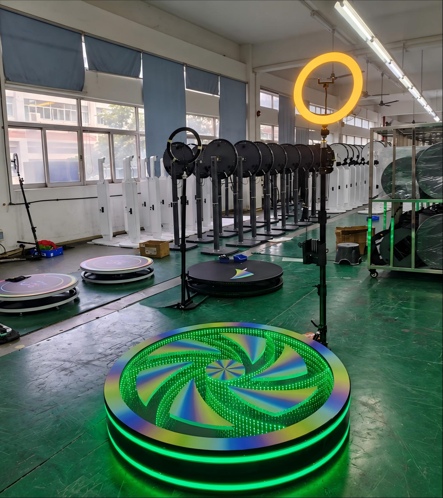 360 photo booth with a green LED infinity mirror platform and illuminated ring light in a factory workshop.