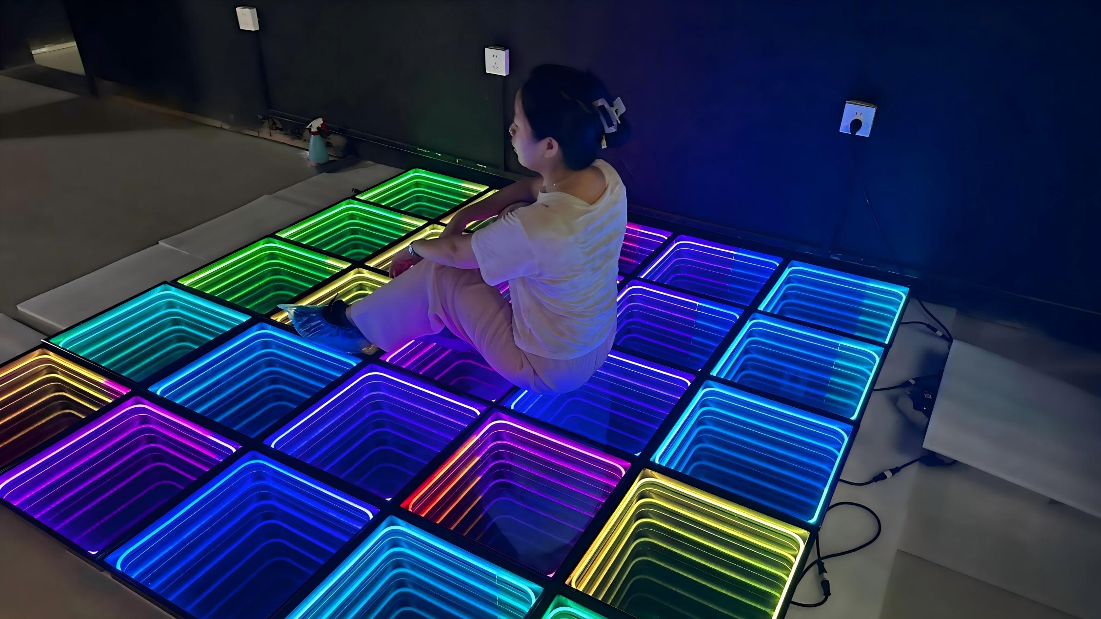 Femme assise sur une piste de danse LED néon multicolore avec des panneaux à miroir infini créant une illusion de profondeur 3D lors d’un test.