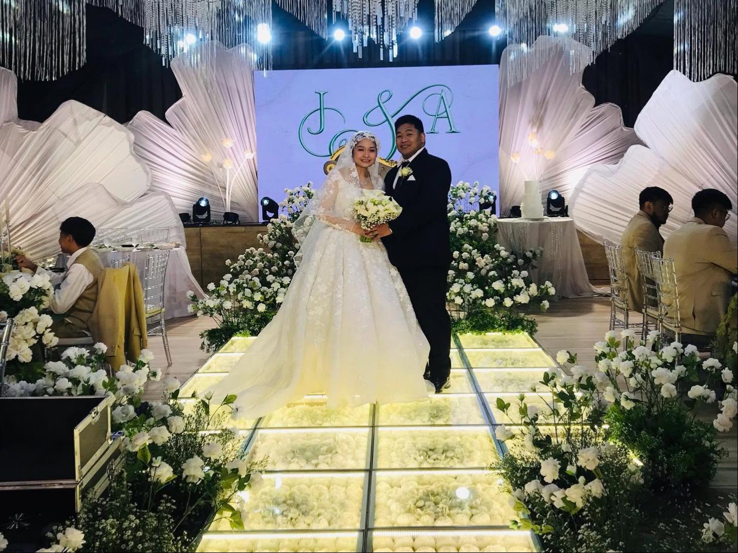 Novios de pie sobre una pista de baile LED floral blanca iluminada durante una recepción de boda de lujo.